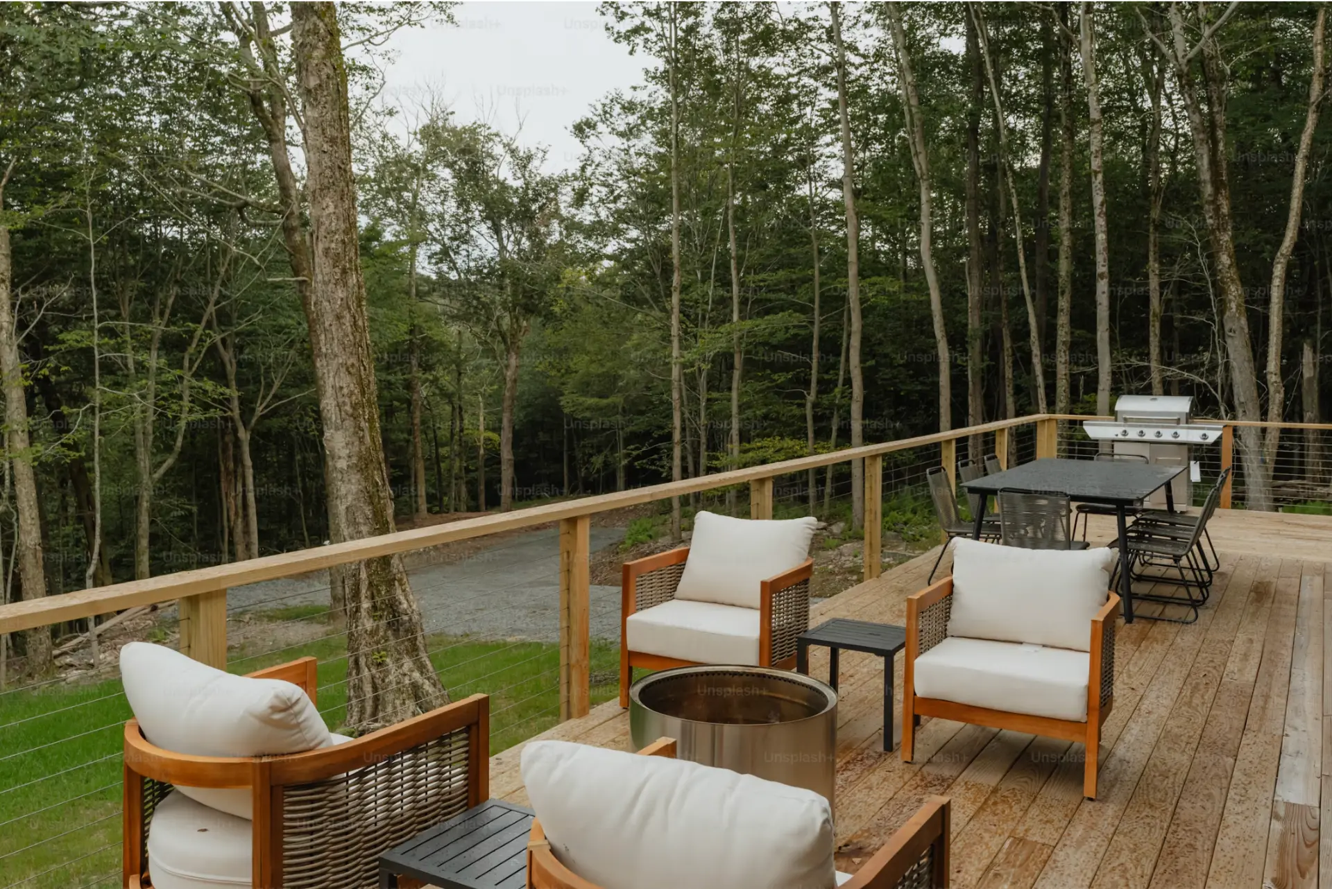 Wood deck with cable railing, lounge chairs and a fire table overlooking a wooded lot
